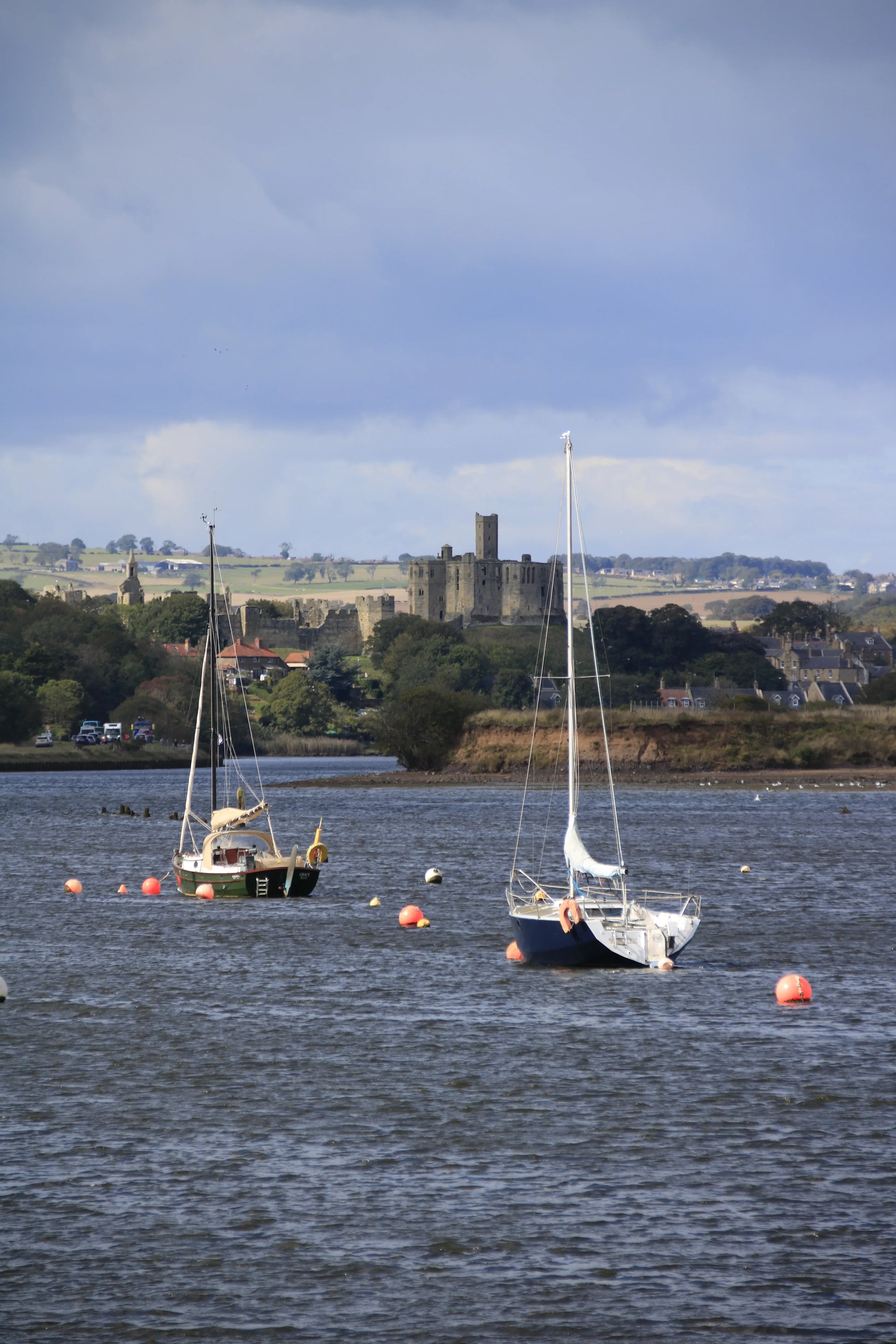 Northumberland coastal landscape with Warkworth Castle, moored sailboats, and buoys in calm water