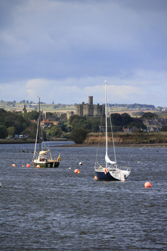 Northumberland coastal landscape with Warkworth Castle, moored sailboats, and buoys in calm water