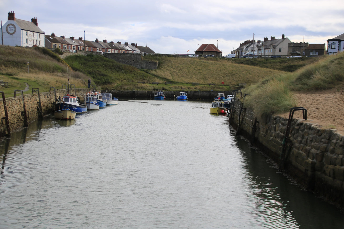 Seaton Sluice Northumberland coastal harbor with moored fishing boats and stone walls under a cloudy sky