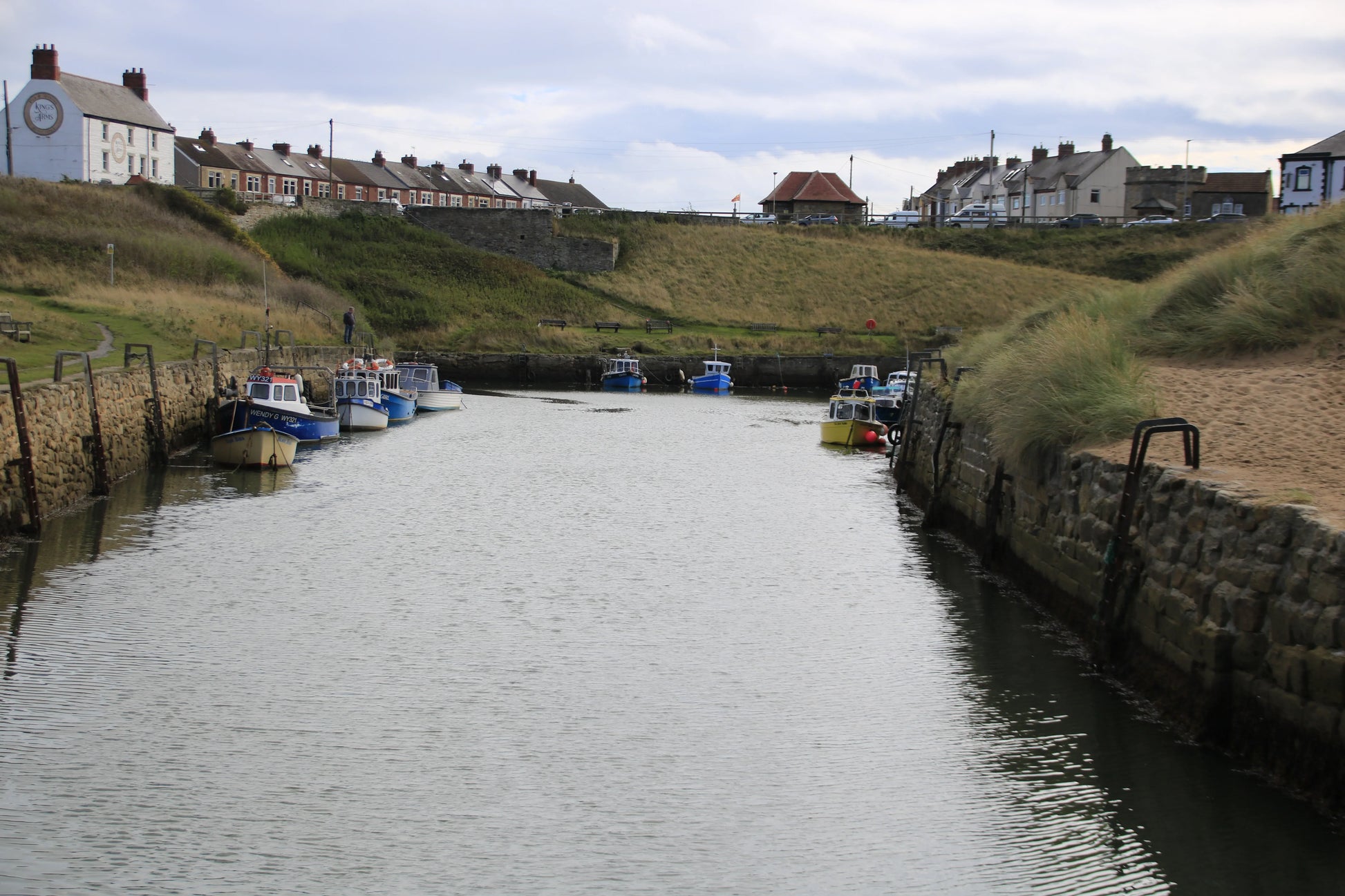 Seaton Sluice Northumberland coastal harbor with moored fishing boats and stone walls under a cloudy sky