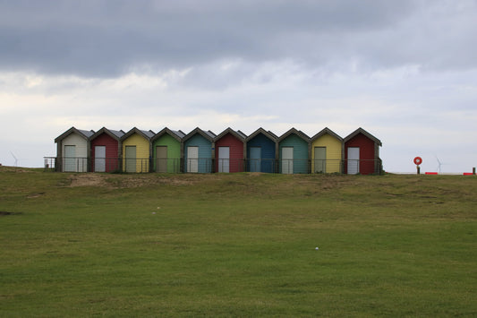 Row of colorful wooden beach huts on grassy hill under overcast sky at Blythe Beach, Northumberland UK