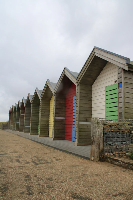 Row of colorful wooden beach huts with gabled roofs on a cloudy day at Blythe Beach, Northumberland