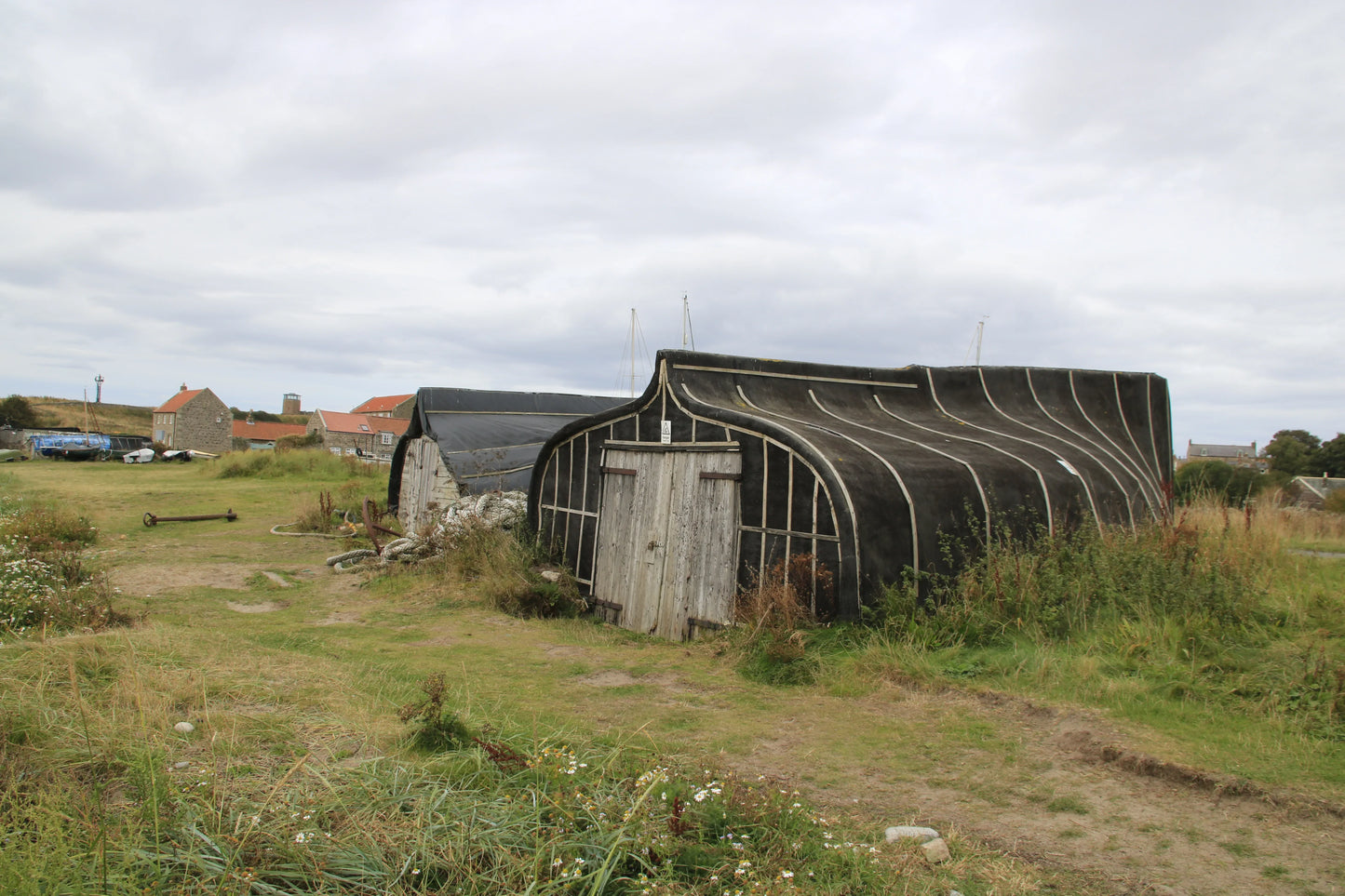 Traditional upturned boat shed with weathered wooden doors in grassy Northumberland coastal village under cloudy sky