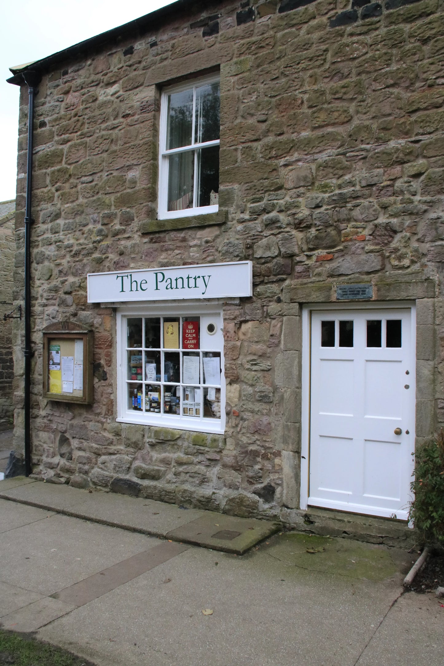 Stone building with white door and window displaying The Pantry shop sign in Northumberland