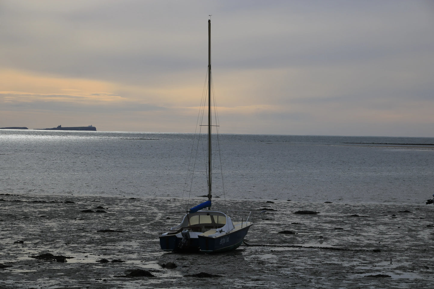 Sailboat grounded on muddy shore at Lindisfarne Harbour, Northumberland, under cloudy sky at dusk