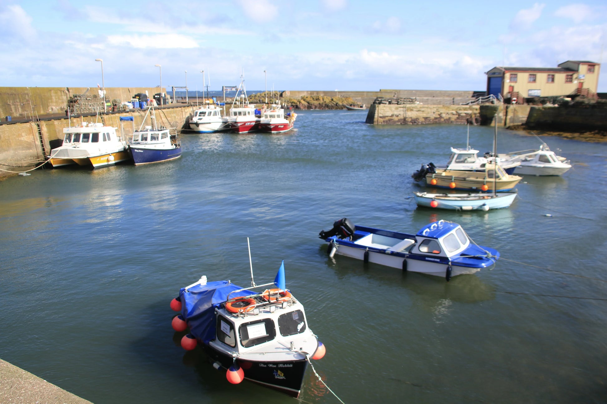 Fishing boats moored in St Abbs harbor, Northumberland, under blue sky and calm waters