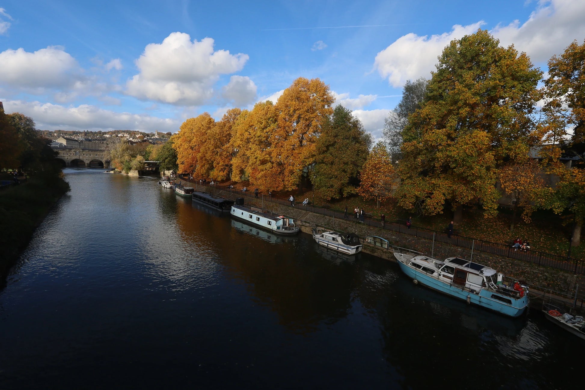Autumn landscape of Bath weir with colorful trees and boats on the river under blue sky