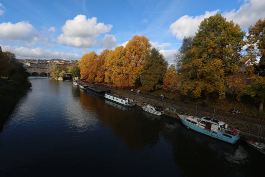 Autumn landscape of Bath weir with colorful trees and boats on the river under blue sky