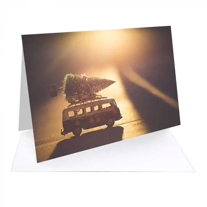Holiday card featuring a toy van carrying a Christmas tree on its roof in warm sunset light