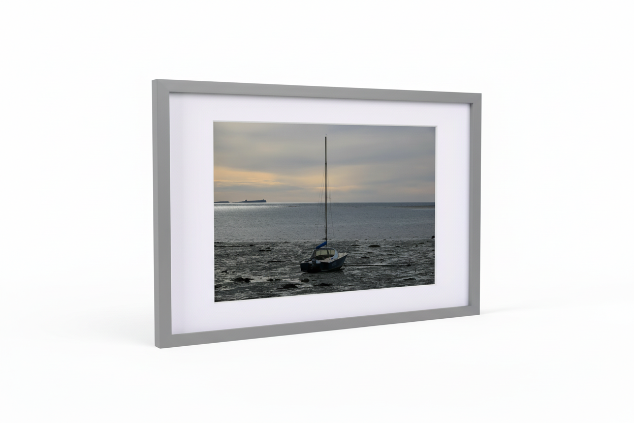 Framed photo print of Lindisfarne Harbor at sunset with sailboat on rocky shore and calm sea